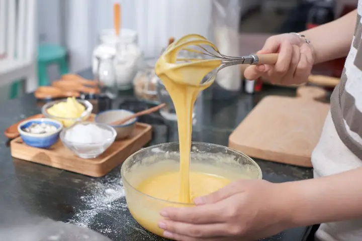 woman whisking a batter in a bowl for no-bake Mango cheesecake recipe