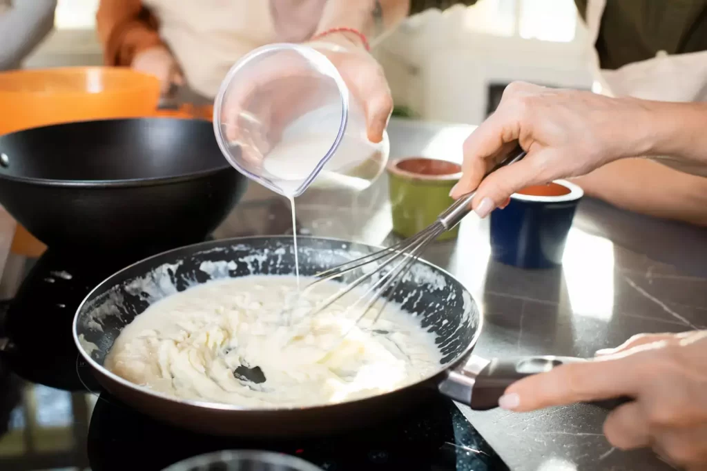 Pouring milk into a pan with cream cheese making a delicious cream cheese sauce.